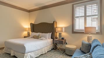 A hotel room with a large bed, two bedside tables with lamps, a small round table, and a blue sofa.
