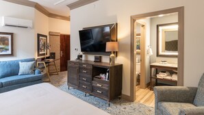 A hotel room with a large bed, a TV, a dresser, a sofa, and a bathroom visible through an open door. - Andrew Pinckney Inn (Charleston)