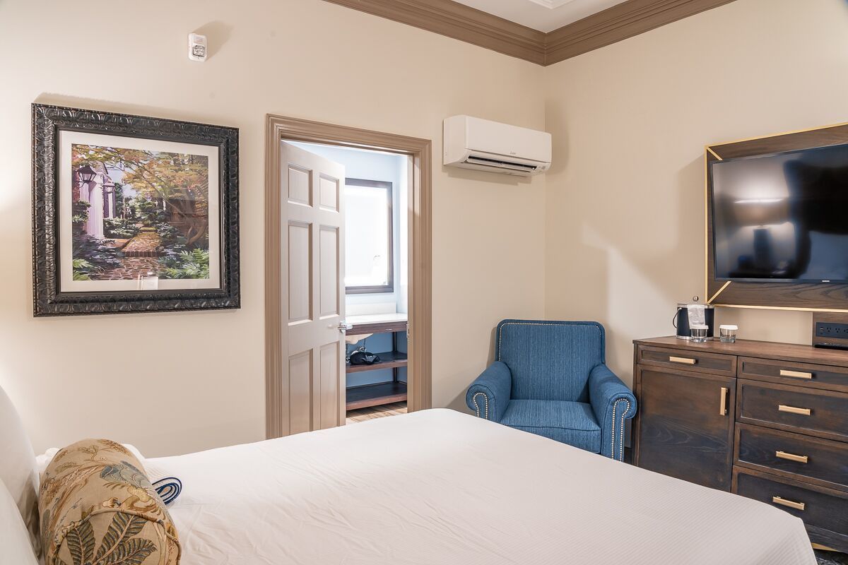 A hotel room with a bed, a blue armchair, a TV, a wardrobe, and a picture on the wall.