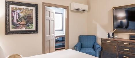 A hotel room with a bed, a blue armchair, a TV, a wardrobe, and a picture on the wall.