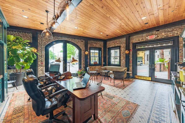 A spacious room with a wooden ceiling, a large desk with a laptop, leather chairs, and a large window with a view of the street. - Andrew Pinckney Inn (Charleston)