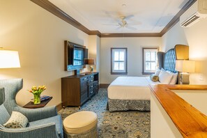 A hotel room with a bed, a desk with a TV, a chair, a dresser, and a ceiling fan.