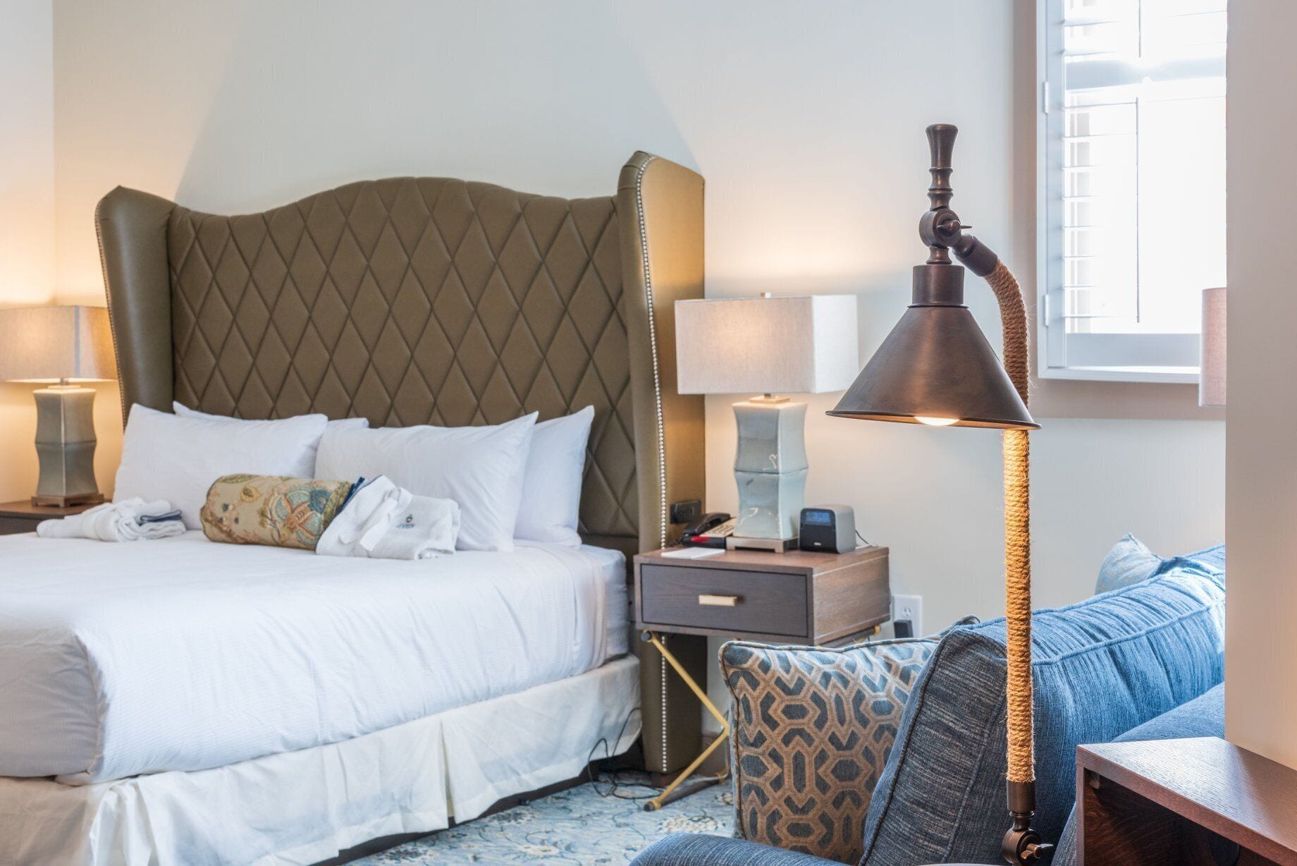 A hotel room with a large bed, two bedside tables, a nightstand, a lamp, and a cat tree.