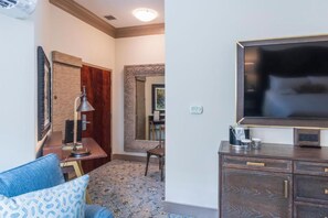 A hotel room with a large flat-screen TV, a desk with a lamp, a chair, and a coffee maker. - Andrew Pinckney Inn (Charleston)