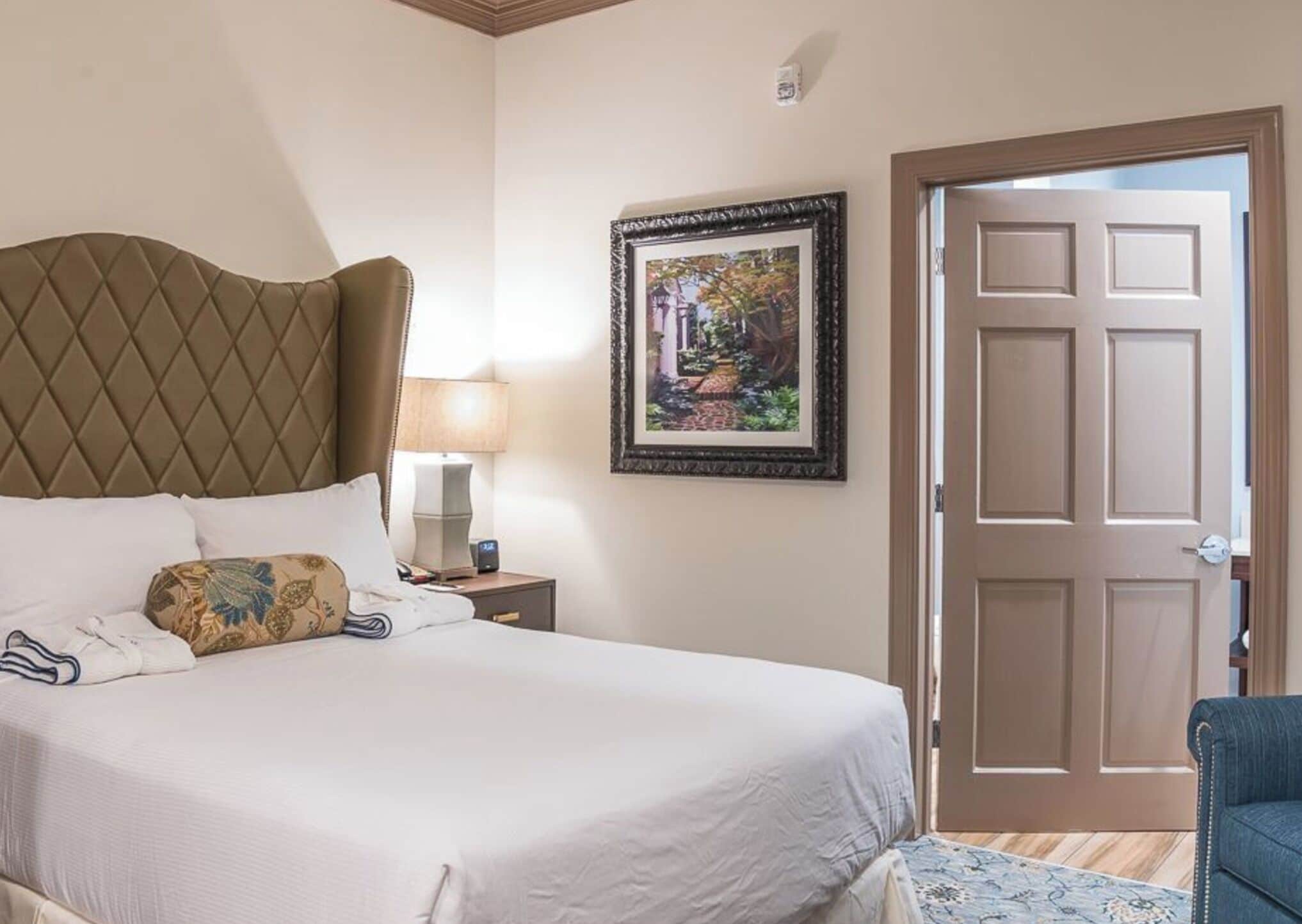 Une chambre d’hôtel avec un lit, une table de chevet, une lampe, un tableau encadré et une porte.