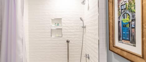 A modern bathroom with a white tiled shower, a bathtub, and a framed picture on the wall.