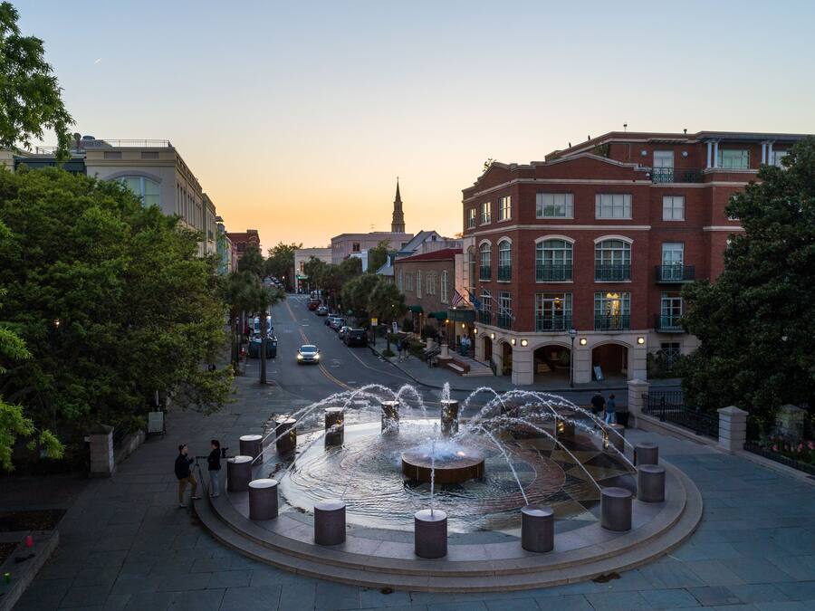 A public square with a central fountain, surrounded by trees and buildings.