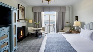 A hotel room with a large bed, a fireplace, a balcony with a view, a TV, and a desk with a chair. - HarbourView Inn (Charleston)