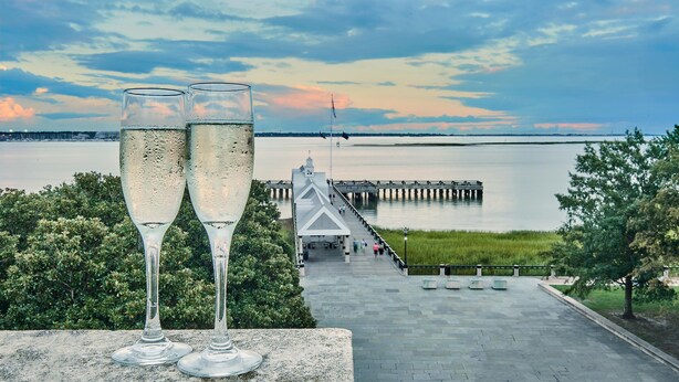 Deux flûtes à champagne sont posées sur une étagère, offrant une vue sur une jetée et une étendue d’eau.