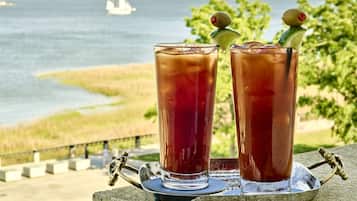 Deux grands verres de thé glacé, décorés de quelques éléments, sont posés sur un plateau. L’ensemble est présenté sur fond de paysage côtier, avec une clôture et des arbres en arrière-plan.