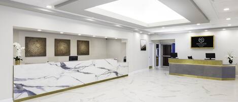 A modern hotel reception area with a marble reception desk, a digital display board, and a skylight ceiling.