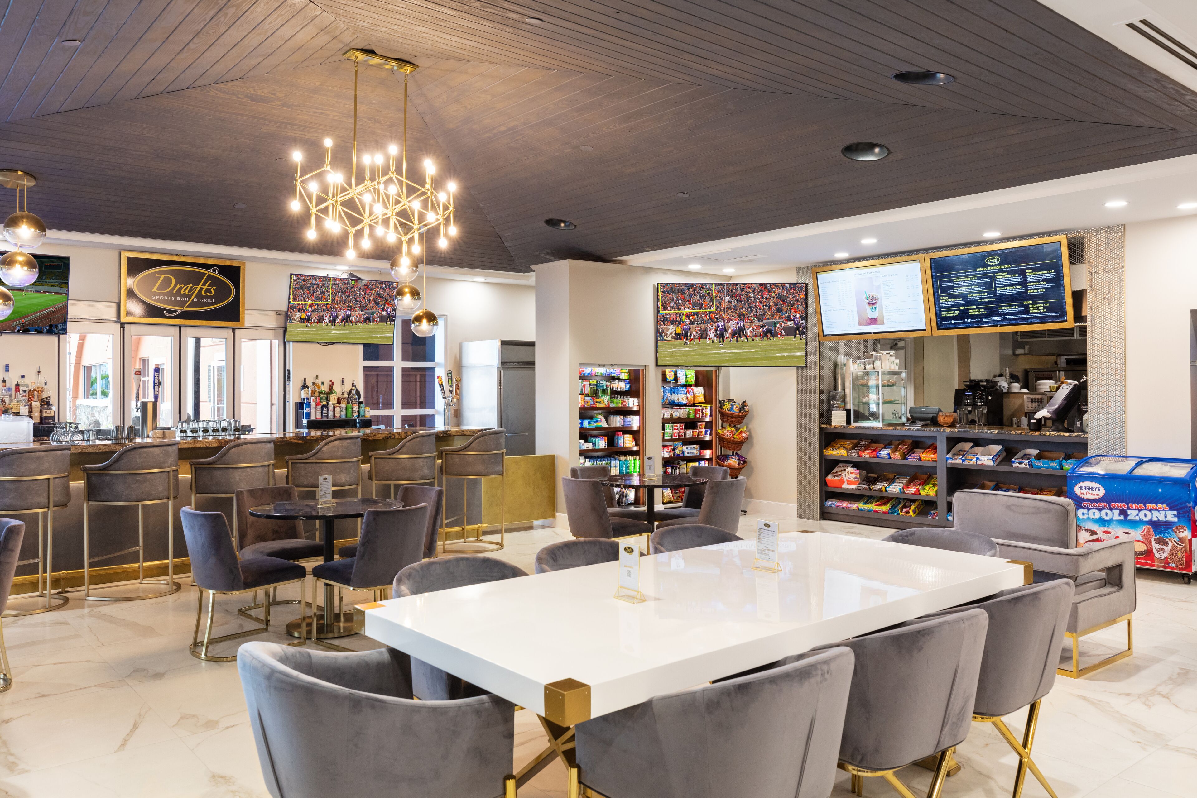 A modern bar area with a white bar counter, grey upholstered chairs, and a chandelier.