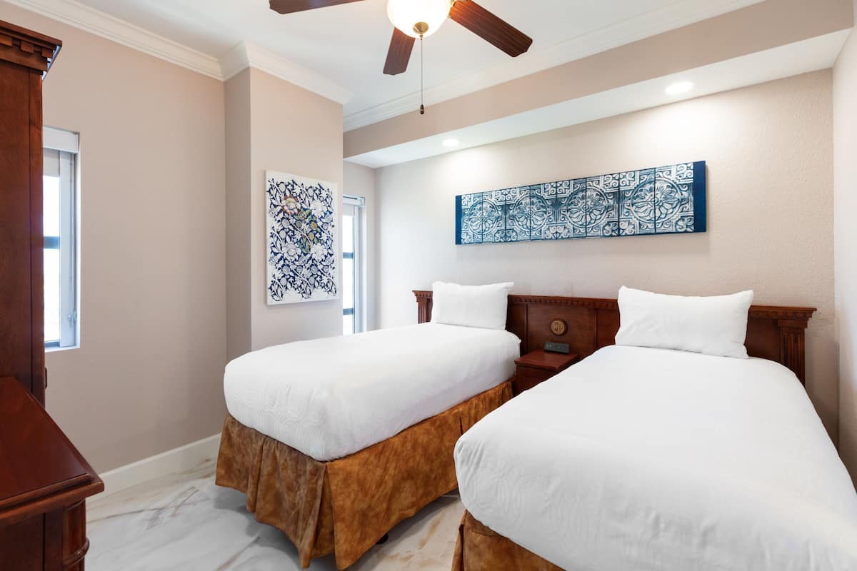 A hotel room with two beds, a ceiling fan, and artwork on the walls.