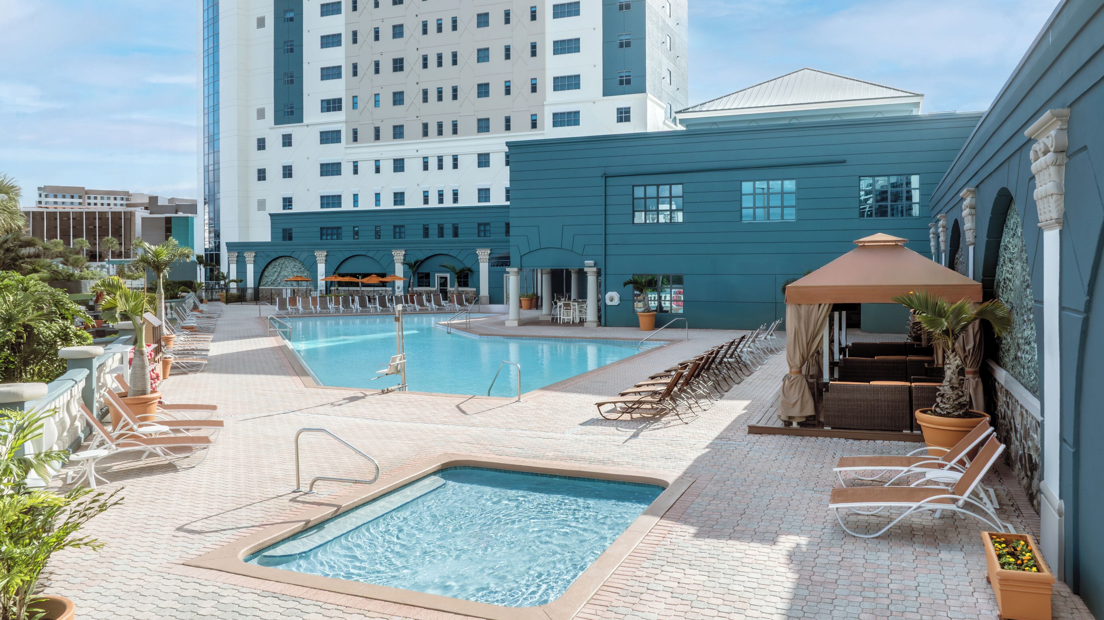 Un espace piscine d’hôtel comprenant deux piscines, des chaises longues et un espace de repos abrité.