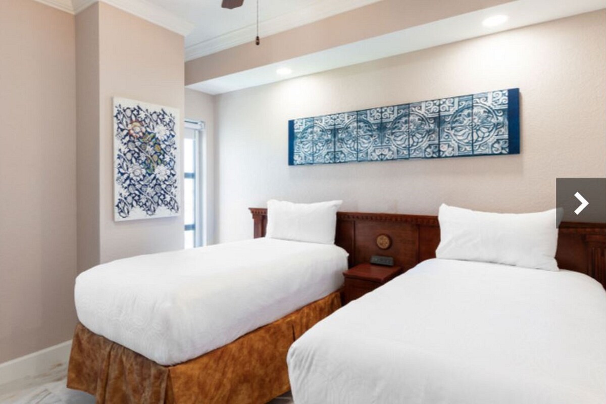 Une chambre d’hôtel avec deux lits, une tête de lit en bois et une grande œuvre d’art aux motifs bleus et blancs accrochée au mur.