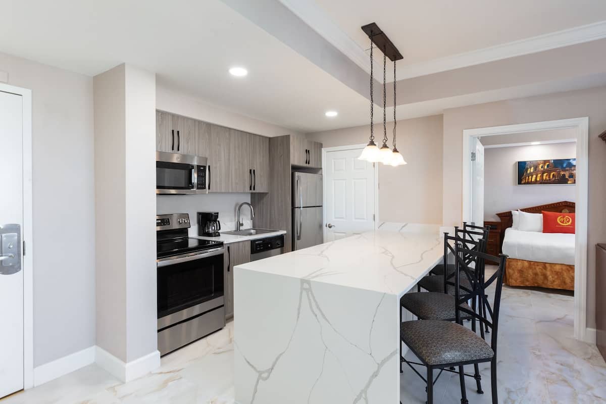 A modern kitchen with a central island, stainless steel appliances, and a dining area with chairs.