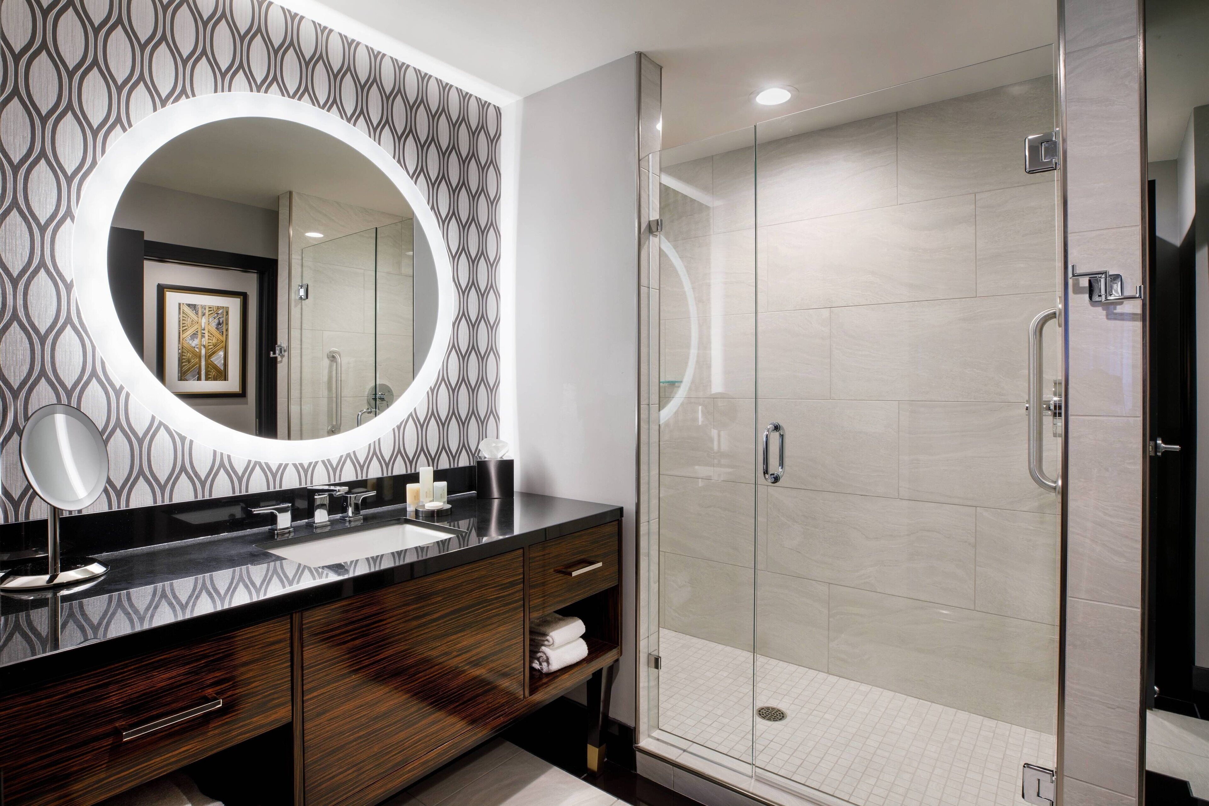 A modern bathroom with a large mirror, a glass-enclosed shower, and a patterned wall.