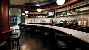 Een bar met een gebogen toonbank, meerdere barkrukken en een televisiescherm.