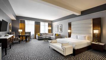 A modern hotel room with a large bed, a sofa, a desk, and a dining area.