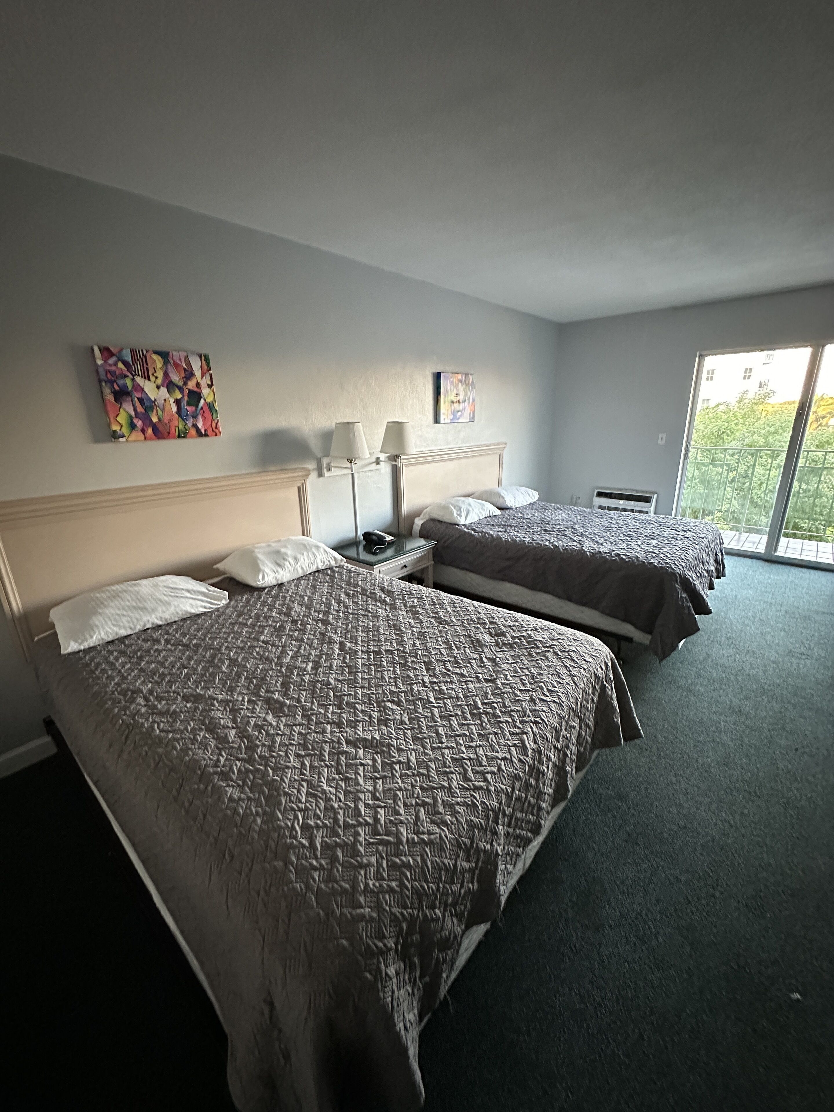 A hotel room with two beds, a large window, and artwork on the walls.