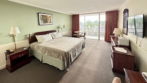 Une chambre d’hôtel comprenant un lit, des tables de chevet, un bureau, une chaise, une télévision et un balcon avec des rideaux.
