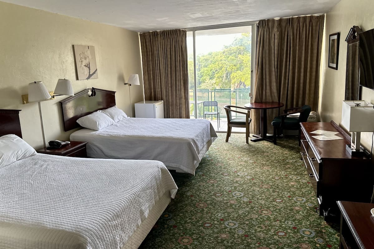 Ein Hotelzimmer mit zwei Betten, einem Schreibtisch, einem Stuhl und einem kleinen Tisch.