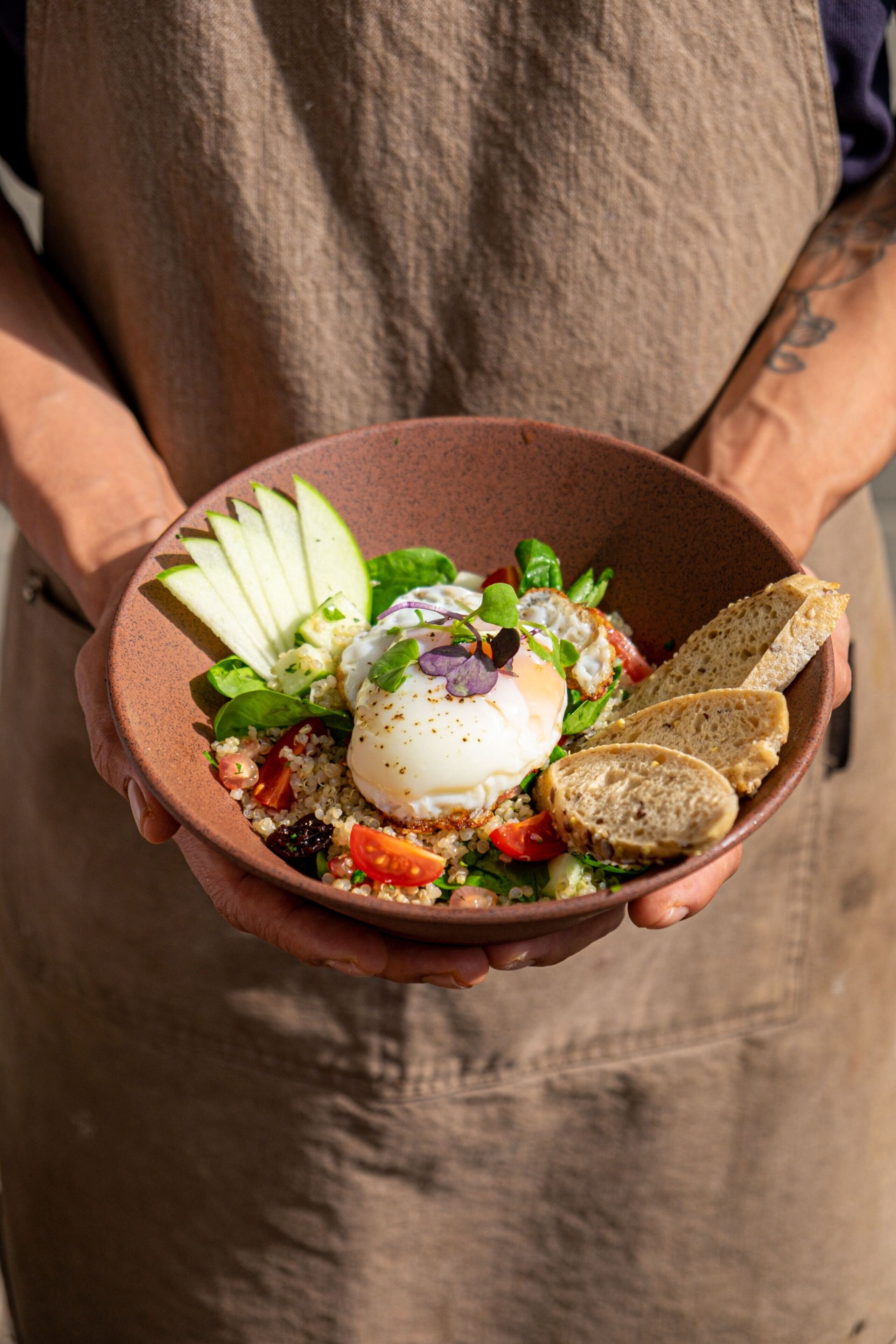 A person holding a bowl of salad with various ingredients and a poached egg.