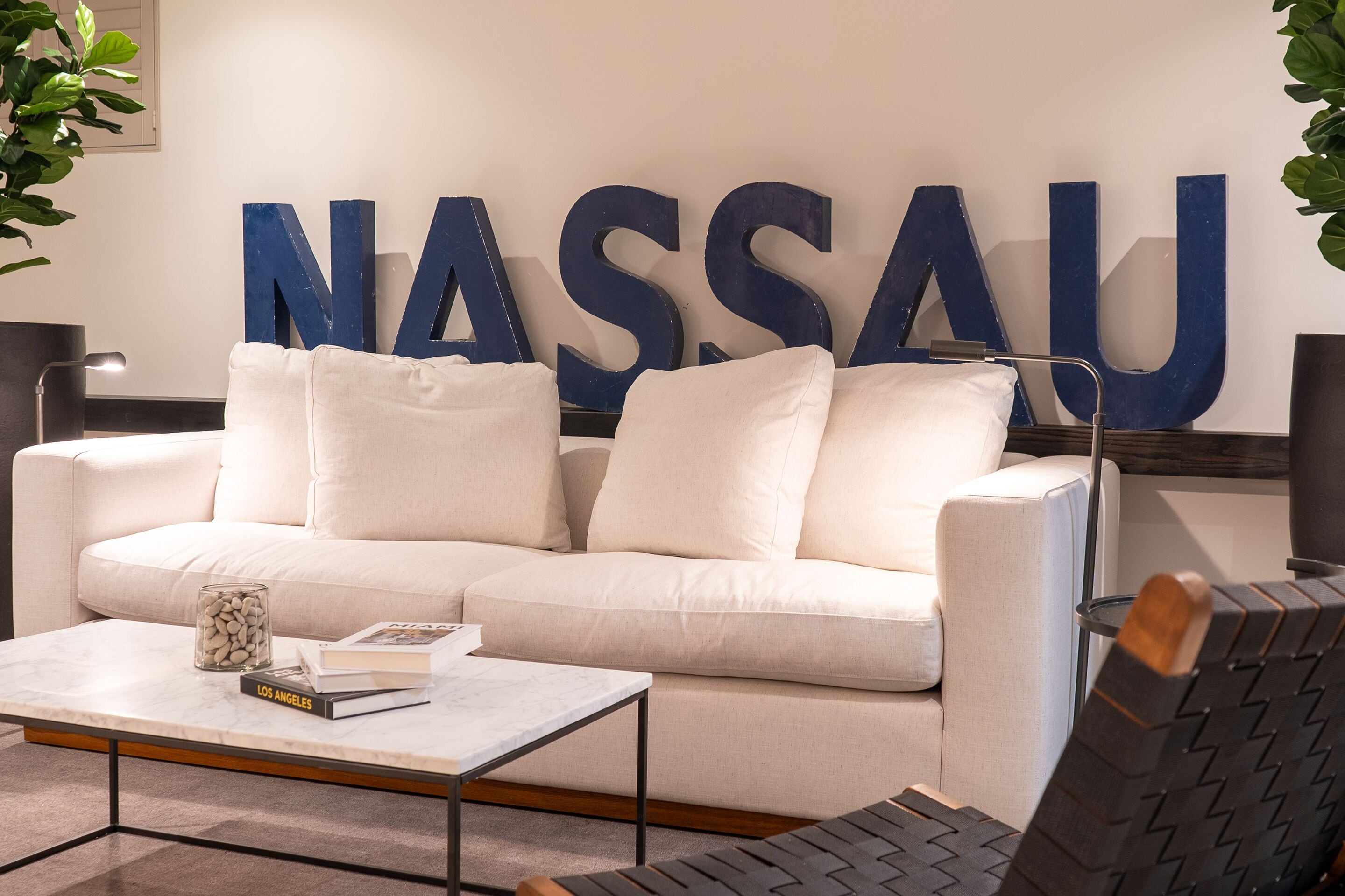 A modern living room with a white sofa, a coffee table, and a large blue sign that reads "NASSAU".