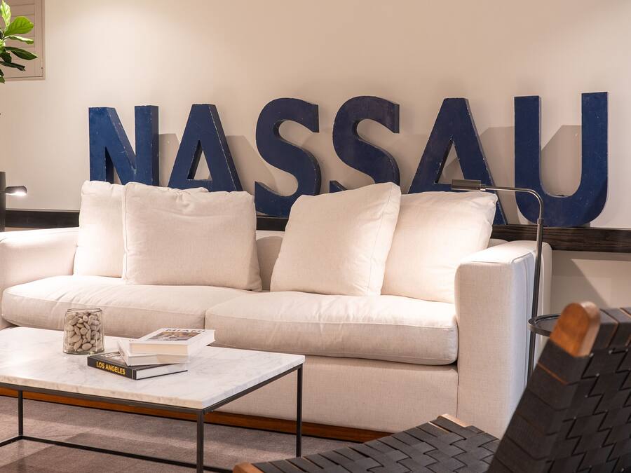 A modern living room with a white sofa, a coffee table, and a large blue sign that reads "NASSAU".