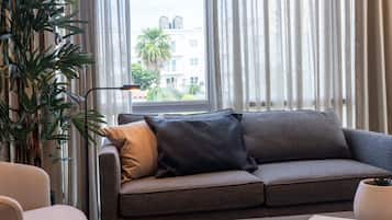 Un salon moderne avec un canapé gris, un fauteuil blanc, une table basse et une grande plante.