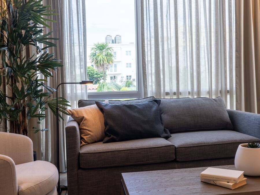 Un salon moderne avec un canapé gris, un fauteuil blanc, une table basse et une grande plante.