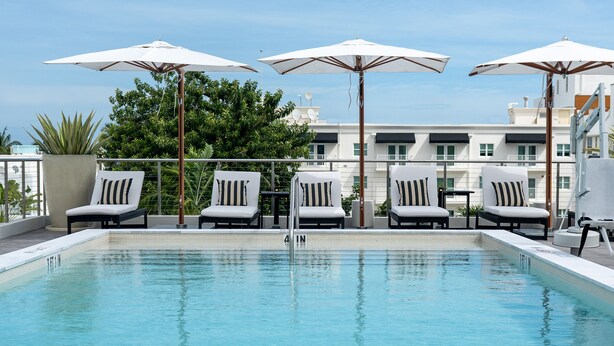A rooftop pool with white lounge chairs and umbrellas, surrounded by greenery and modern buildings. - Nassau Suite South Beach, an All-Suite Hotel (Miami Beach)