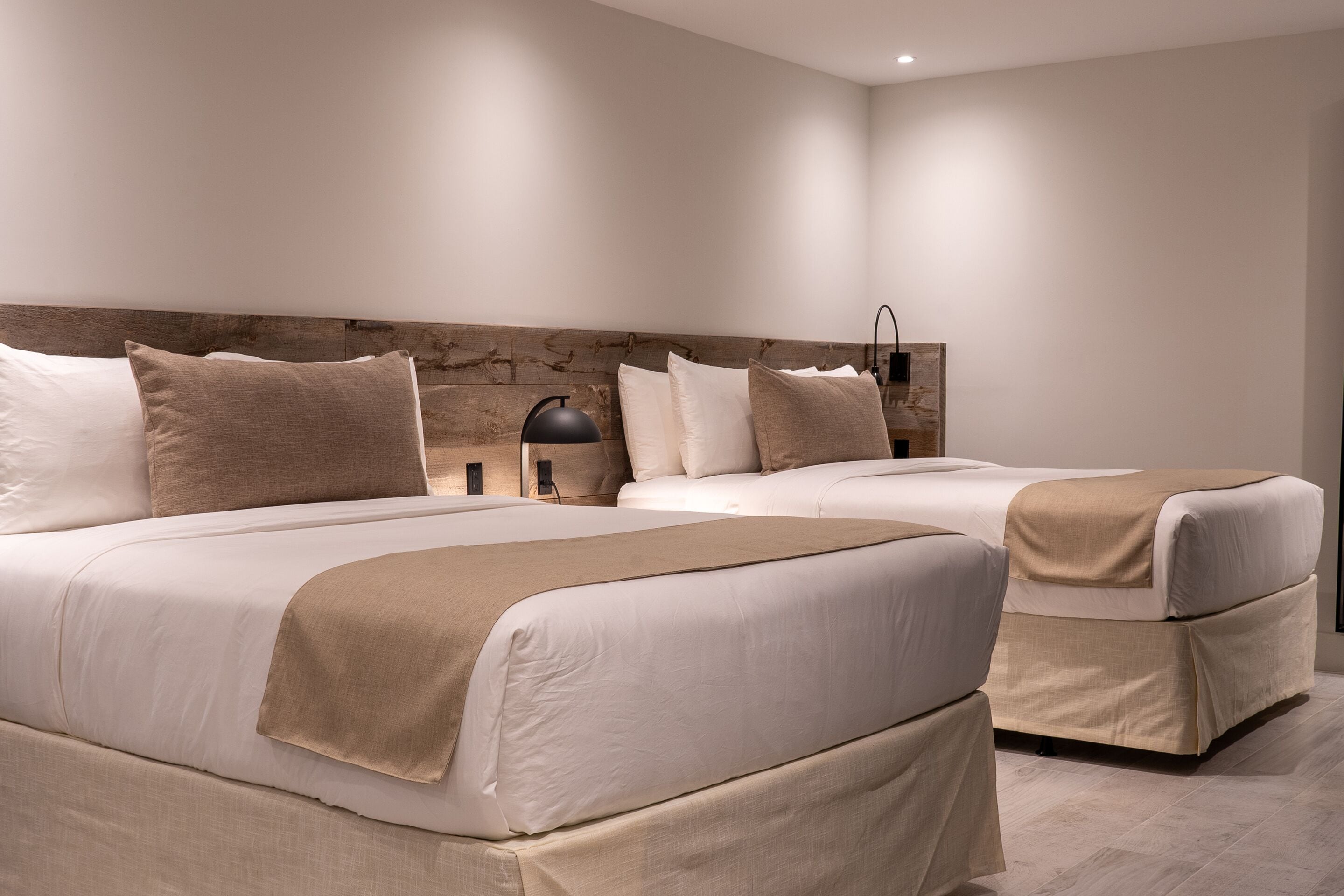 A modern bedroom with two beds, a wooden headboard, and a bedside table with a lamp.