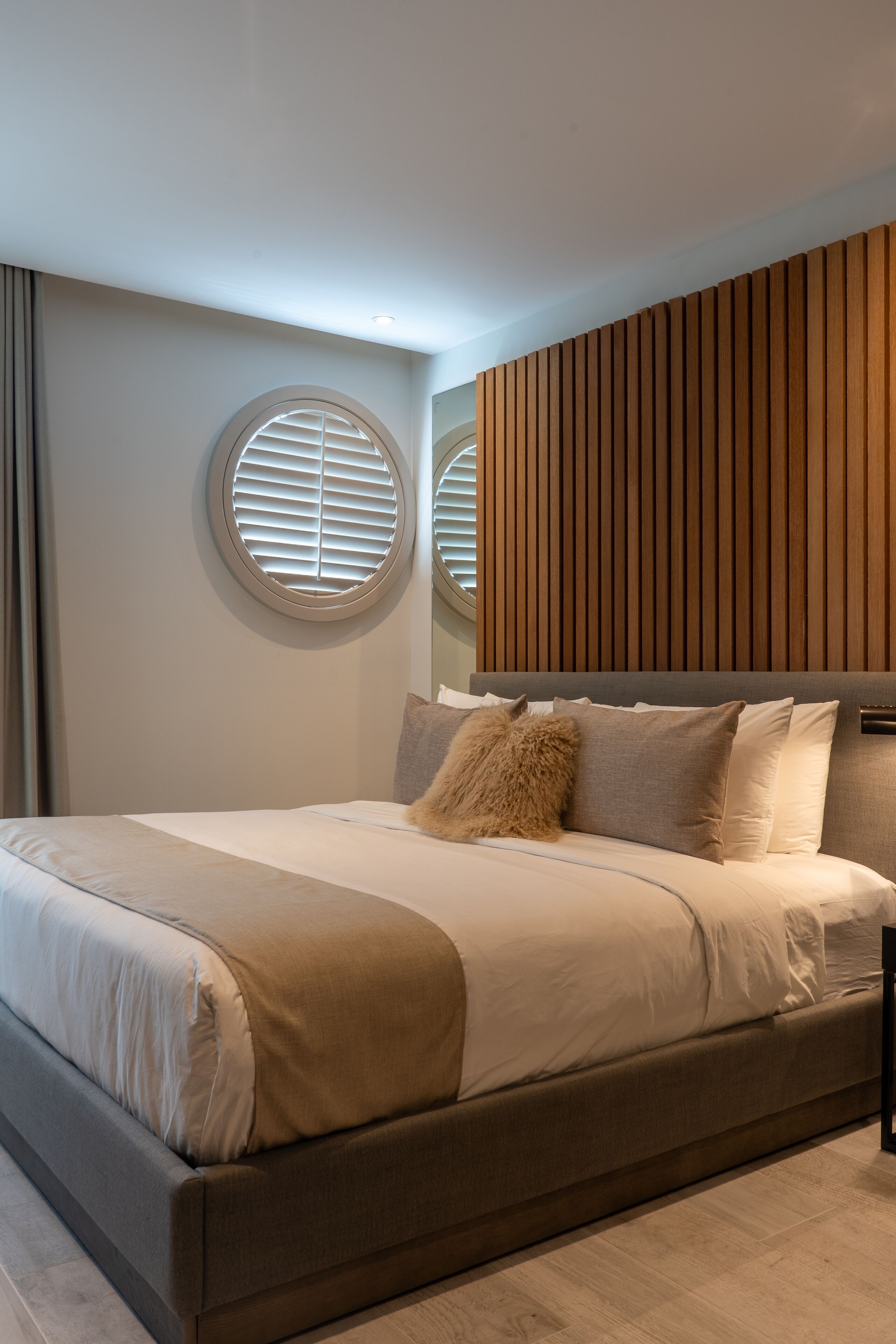 Une chambre moderne avec un grand lit, des fenêtres rondes encastrées dans le mur et un mur recouvert de panneaux en bois.