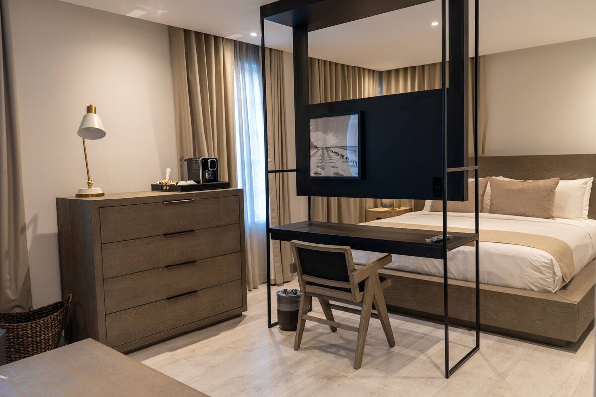 A modern hotel room with a bed, desk, chair, and a television on the wall.