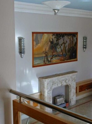 Een kamer met een open haard, een schilderij en wandlampen.