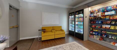 A modern living room with a mustard-colored sofa, a white abstract painting, and a large beverage refrigerator stocked with various drinks.