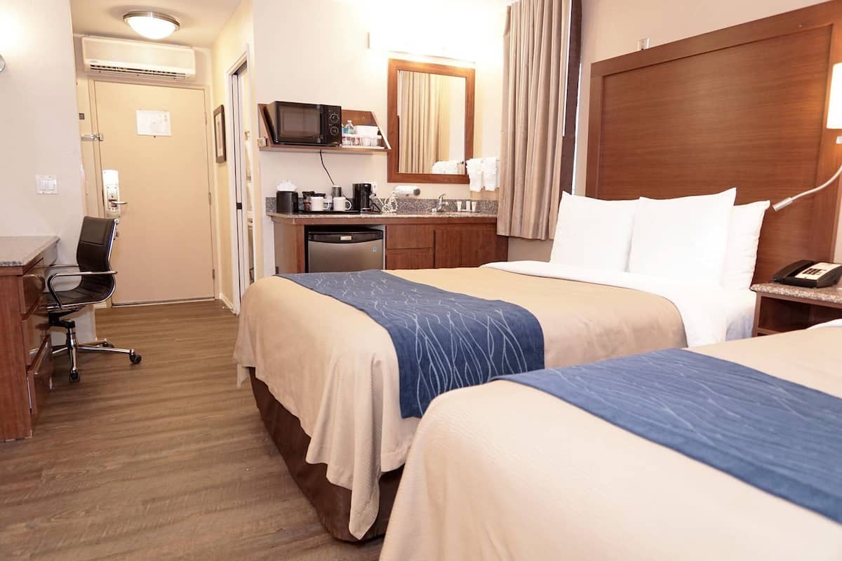 A hotel room with two beds, a desk with a chair, a microwave, a coffee maker, a sink, and a telephone.