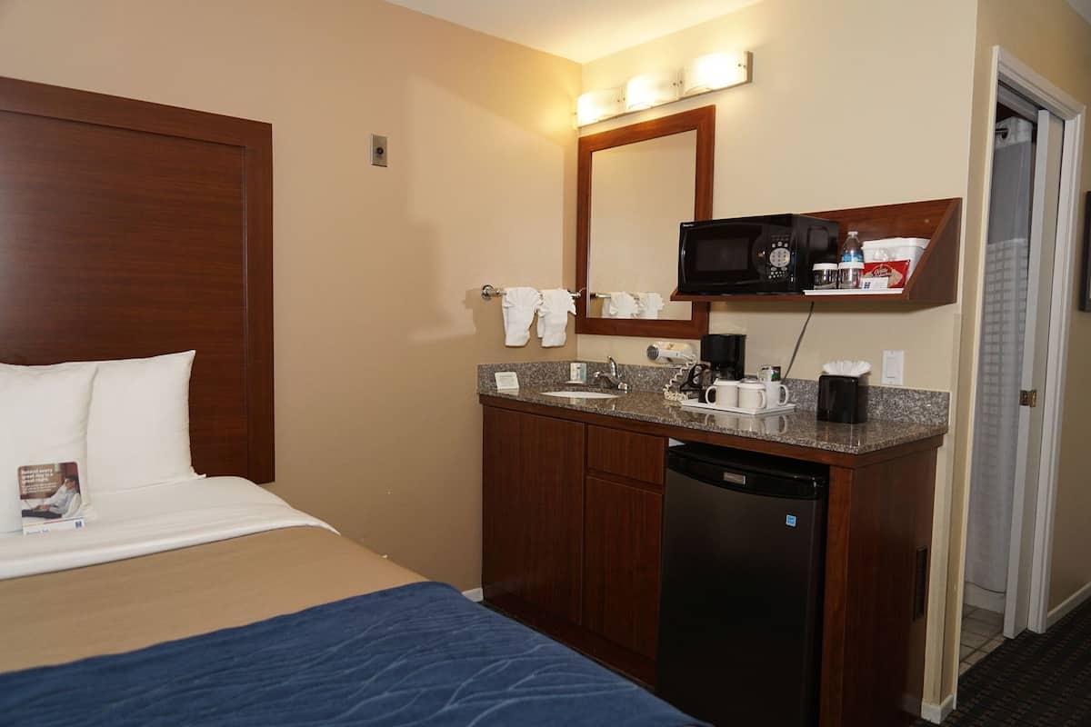 A hotel room with a bed, a bathroom with a sink, a mirror, a microwave, and a coffee maker.