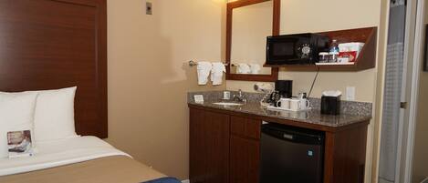 A hotel room with a bed, a bathroom with a sink, a mirror, a microwave, and a coffee maker.