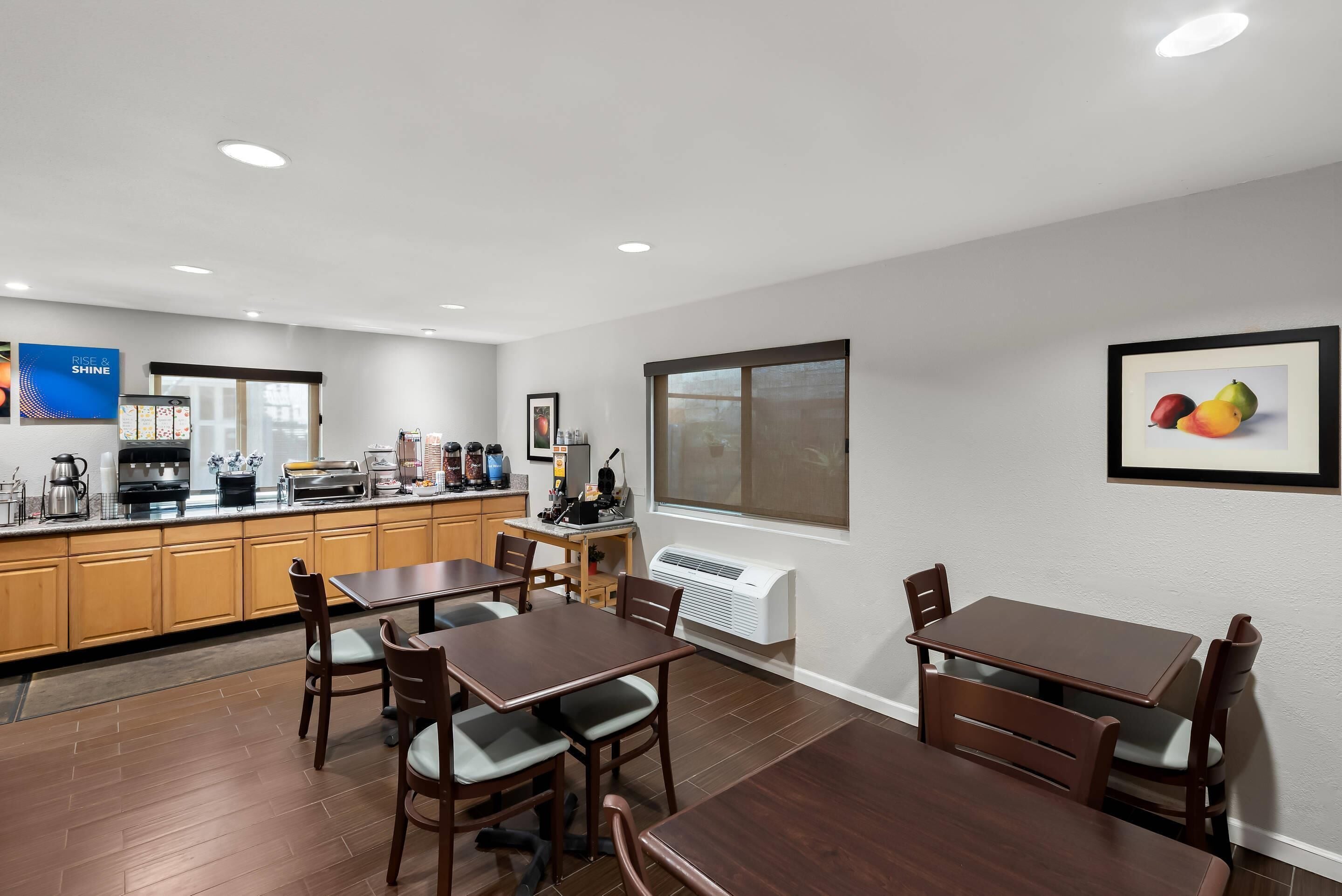 Una cocina moderna con armarios de madera, una zona de café y un comedor con mesas y sillas de madera.