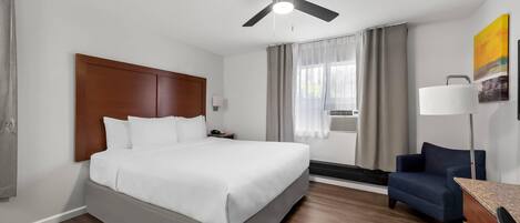 Une chambre d’hôtel avec un grand lit, un ventilateur de plafond, un bureau avec une lampe, une chaise et un tableau au mur.