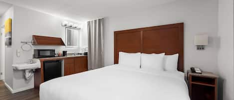 A hotel room with a large bed, a wooden headboard, a small desk with a telephone, a sink, and a microwave.