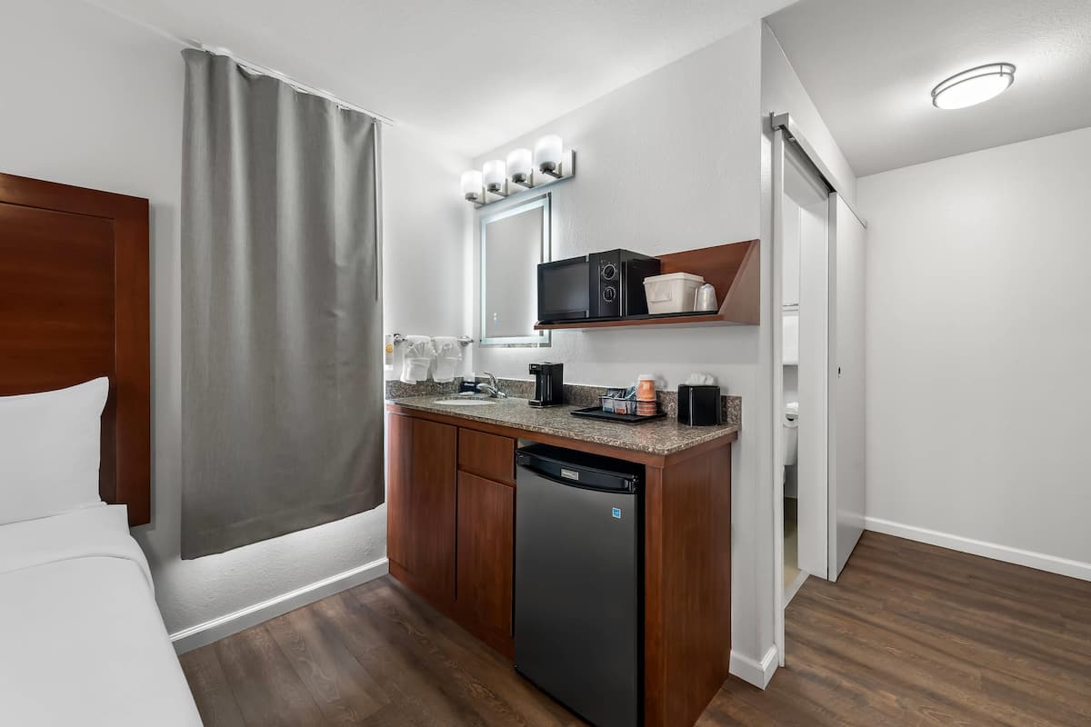 A compact hotel room with a bed, a small kitchenette, a microwave, a coffee maker, and a dishwasher.
