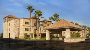 A multi-story hotel with stone facade, palm trees, and a covered outdoor area. - Ayres Suites Diamond Bar (Diamond Bar)