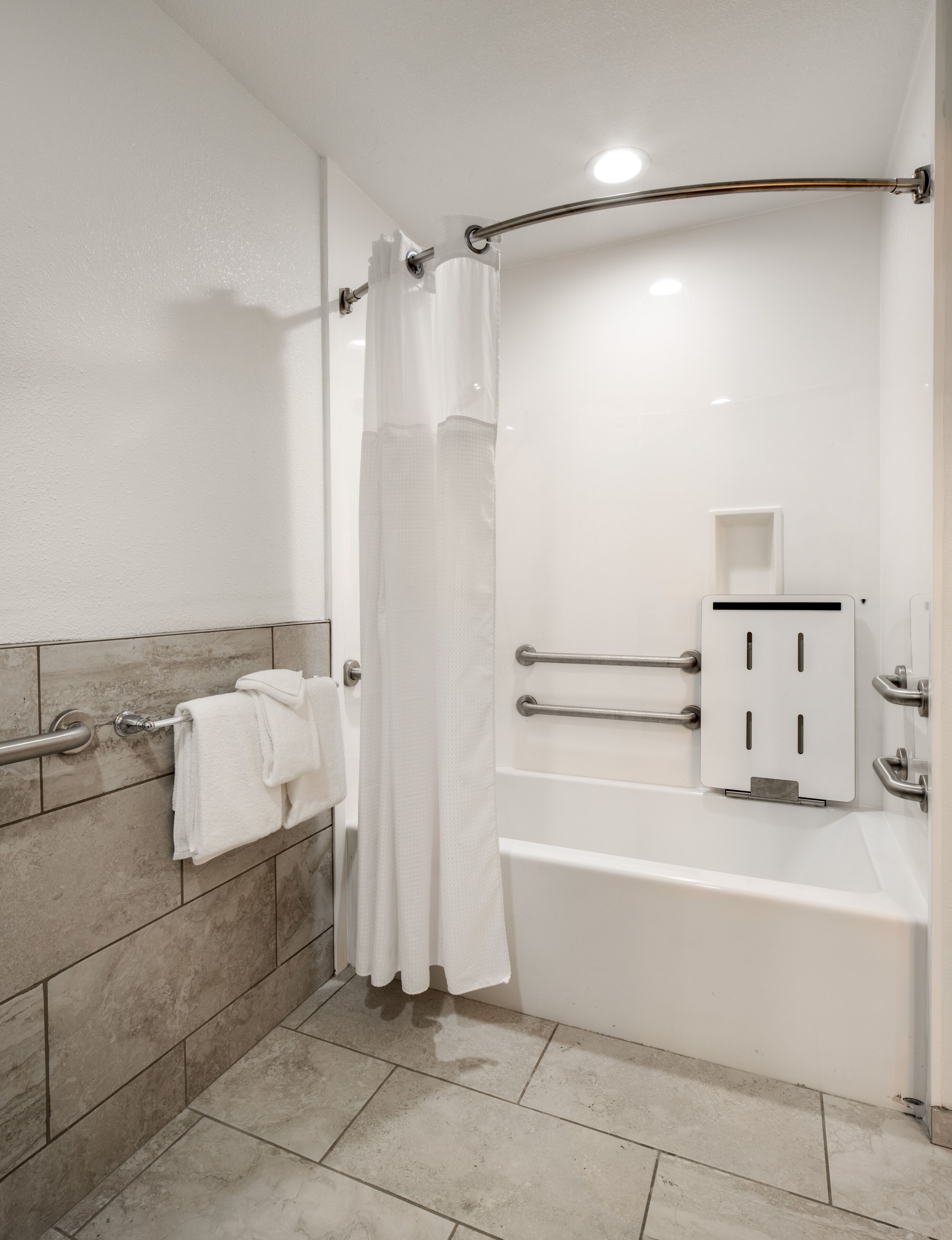 A modern bathroom with a bathtub, a shower curtain, a towel rack, and a handrail.