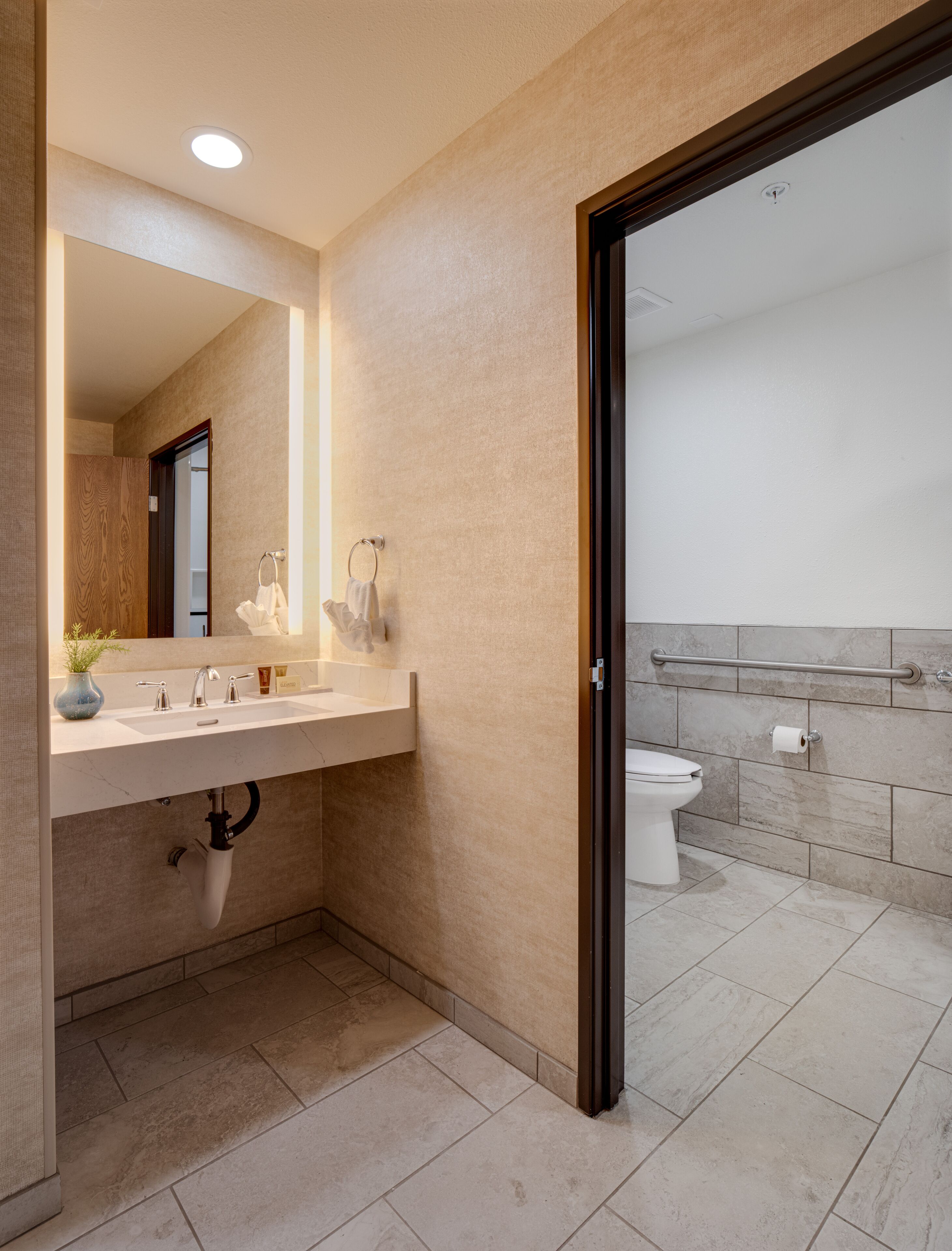 A modern bathroom with a large mirror, a sink with two faucets, a toilet, and a shower area.