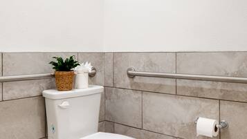 Un bagno moderno con il water bianco, un mancorrente, una pianta in vaso e un portasciotto.