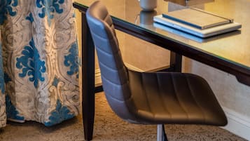 A modern hotel room with a glass desk, a laptop, a notebook, a coffee cup, and a decorative curtain.