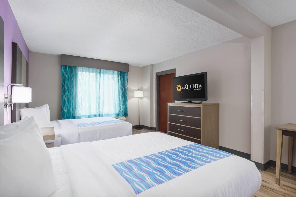 Habitación de hotel con dos camas, televisión, escritorio y ventana con cortinas.
